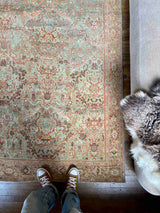 Person standing on a hand-knotted antique Persian Mahal area rug with allover botanical motifs on a celadon green field