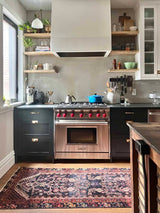 Modern kitchen with stainless steel oven, dark blue cabinets, and vintage Persian Hamadan runner rug with brick red and peach herati motif and navy blue field