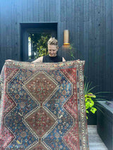 Woman holding an antique hand-knotted Persian area rug with a geometric medallion pattern, featuring a bird motif