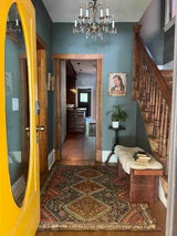 Antique hand-knotted area rug with a geometric medallion pattern in a entryway with wooden bench and chandelier