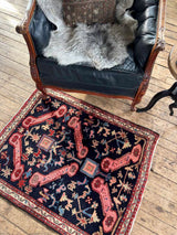 Vintage Caucasian Kuba accent rug with animal motifs on a wooden floor next to a leather chair.