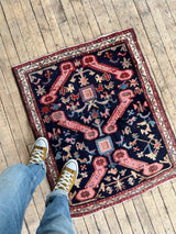 Person standing on a Vintage Caucasian Kuba accent rug with animal motifs on a wood floor