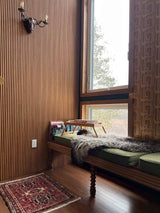 Nook with wooden bench, cushions, red vintage Persian rug, and a window with geometric wallpaper.