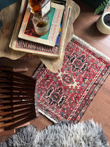 Wooden table with books and a glass of whiskey on a red vintage Persian rug.