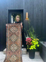 Person holding a vintage Persian runner rug with ivory repeating medallions and a bird and boteh motif on a brick red field