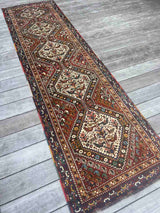 A vintage Persian runner rug with ivory repeating medallions and a bird and boteh motif on a brick red field