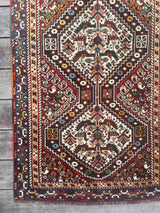 Corner of a vintage Persian runner rug with ivory repeating medallions and a bird and boteh motif on a brick red field