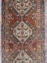 Close-up details of a vintage Persian runner rug with ivory repeating medallions and a bird and boteh motif on a brick red field