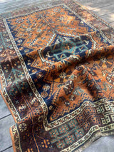 A hand-knotted vintage Persian rug with a geometric pattern, draped on a wood floor