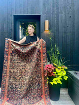 Person holding an Antique Persian area rug with an allover motif on navy field
