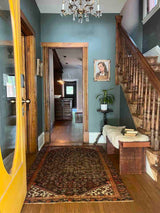 An entryway with staircase, antique art, bench, and an Antique Persian area rug with an allover motif on navy field