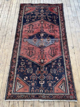 Vintage Persian Saveh area rug with dusty pink and blue geometric designs and a navy field on a wooden floor