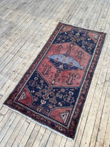Vintage Persian Saveh area rug with dusty pink and blue geometric medallions and a navy field on a wooden floor