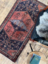 Vintage Persian Saveh area rug with dusty pink and blue medallions and a navy field with a navy leather chair and sheepskin