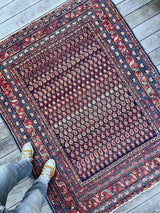 Person standing on an Antique Persian area rug with boteh motifs