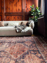 Library with a beige sofa, sheepskin thrrow, and a hand-knotted antique Persian Afshar area rug with medallions 