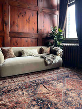 Living room with a beige sofa, Hand-knotted antique Persian Afshar area rug, and wooden panel walls.