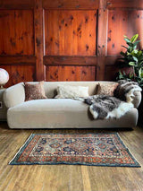 Antique Persian accent rug  with a Beige sofa and a fur throw  in a room with wood paneled walls.