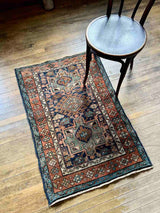 Antique Persian accent rug with intricate patterns on a wooden floor next to a chair.