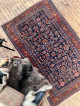 Antique Persian area rug with leather chair and sheepskin at Woven Kin Home