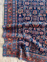 Antique Persian area rug on a wood floor at Woven Kin Home