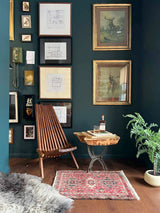 Living room with dark walls, vintage Karajah geometric rug, framed artwork, a wooden chair, and a small table.