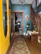 Entryway with yellow door, staircase, antique art, and a vintage Persian runner rug with ivory repeating medallions and a bird and boteh motif on a brick red field
