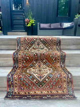 A vintage Persian runner rug with ivory repeating medallions and a bird and boteh motif on a brick red field draped over a stairway