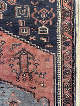 Close-up of a vintage Persian  rug with intricate designs on a dark blue field with dusty pink medallions